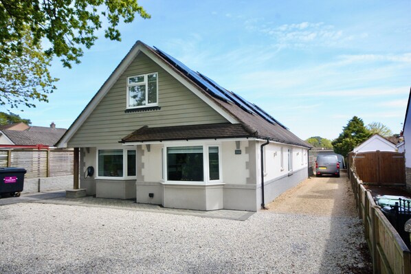 A single-story house with a sloped roof, a garage, and a gravel driveway. - Four Corners Holiday Home with Hot Tub & Sauna (Ferndown)