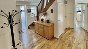 A spacious living area with hardwood flooring, a wooden staircase, and a built-in bench with decorative plants. - Four Corners Holiday Home with Hot Tub & Sauna (Ferndown)