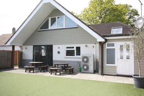 A two-story house with a sloped roof, a patio with wooden tables and benches, and a satellite dish. - Four Corners Holiday Home with Hot Tub & Sauna (Ferndown)