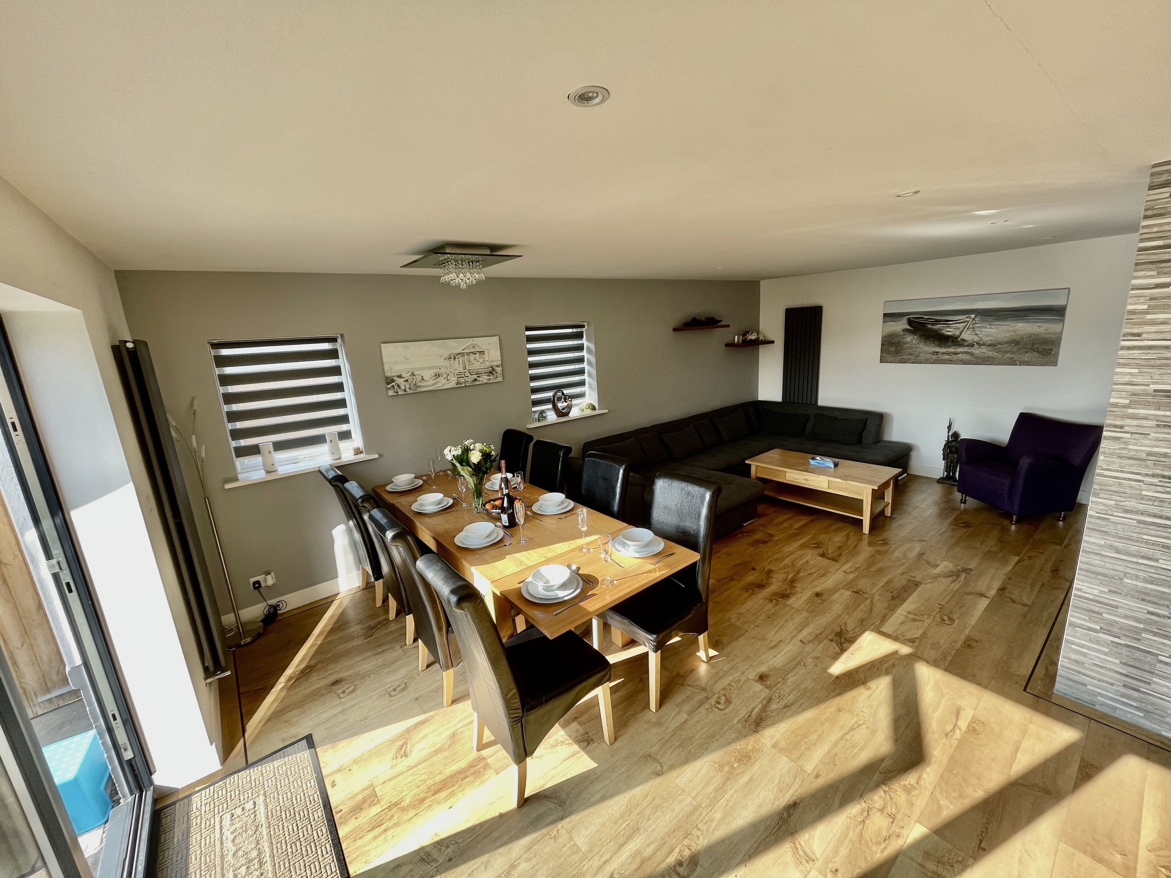 A spacious living area with a dining table set for four, a dark-colored sofa, a wooden coffee table, and a purple armchair.