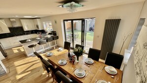 A modern kitchen with white cabinets and a dining area with a wooden table set for four. - Four Corners Holiday Home with Hot Tub & Sauna (Ferndown)
