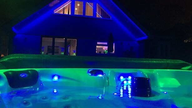 A house with a hot tub in front, illuminated by blue and green lights. - Four Corners Holiday Home with Hot Tub & Sauna (Ferndown)