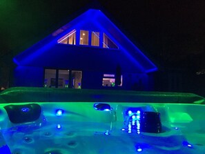 A house with a hot tub in front, illuminated by blue and green lights. - Four Corners Holiday Home with Hot Tub & Sauna (Ferndown)