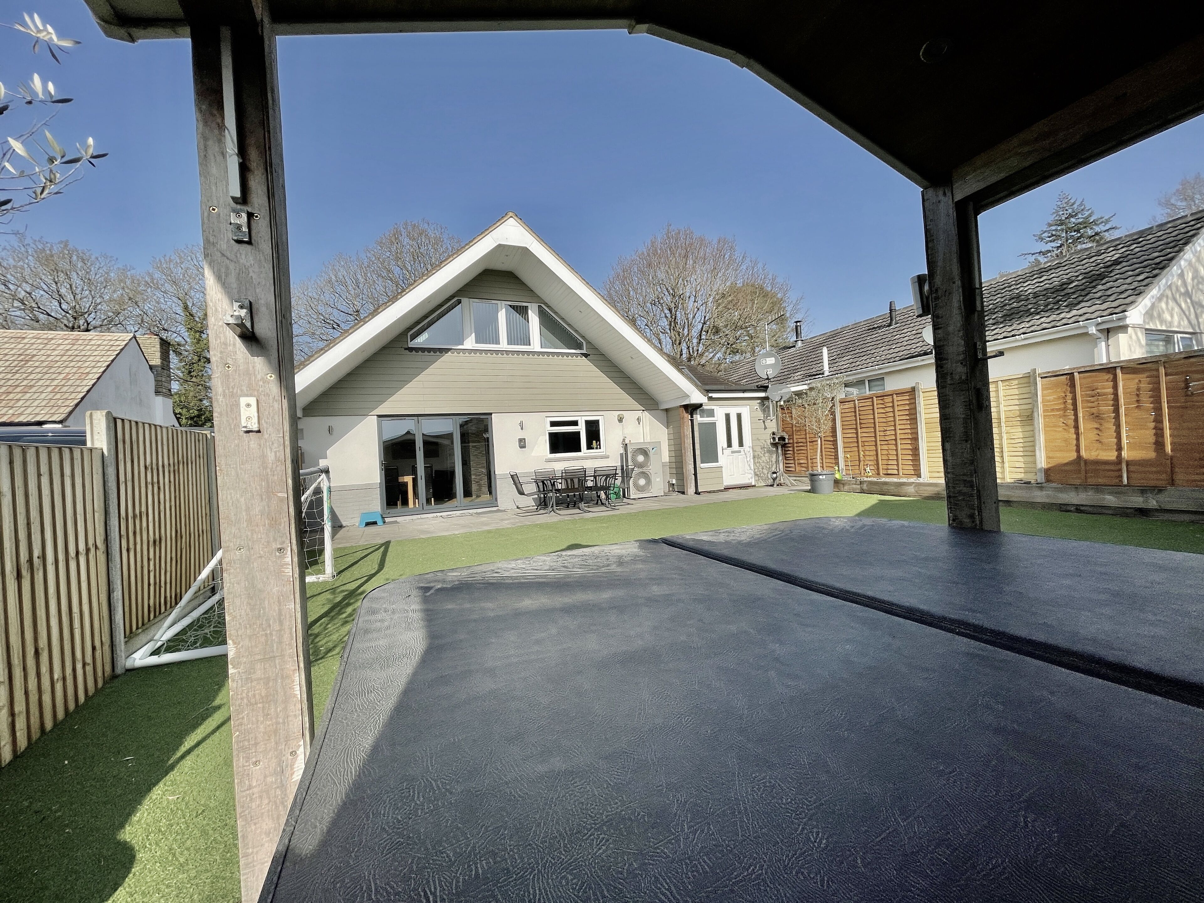 A residential backyard with a trampoline, a wooden fence, and a house with a sloped roof.