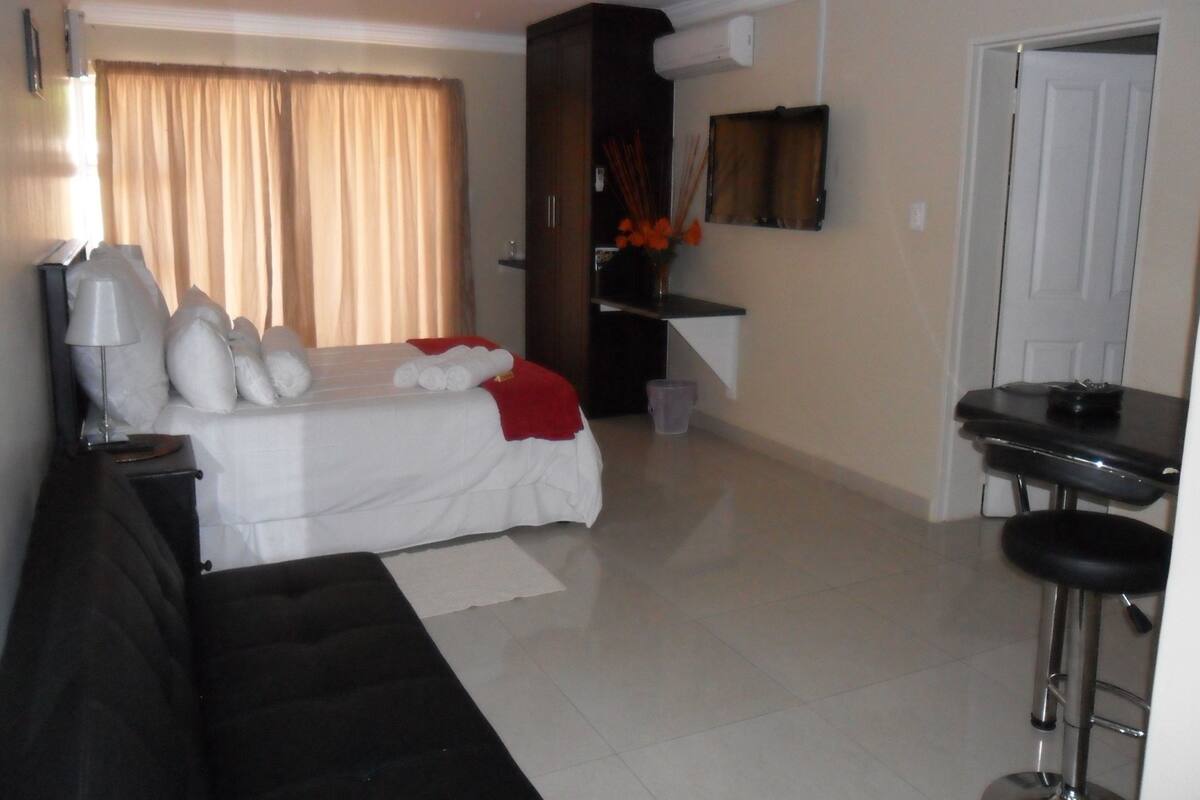 A hotel room with a bed, a desk, a chair, a TV, and a window with curtains.