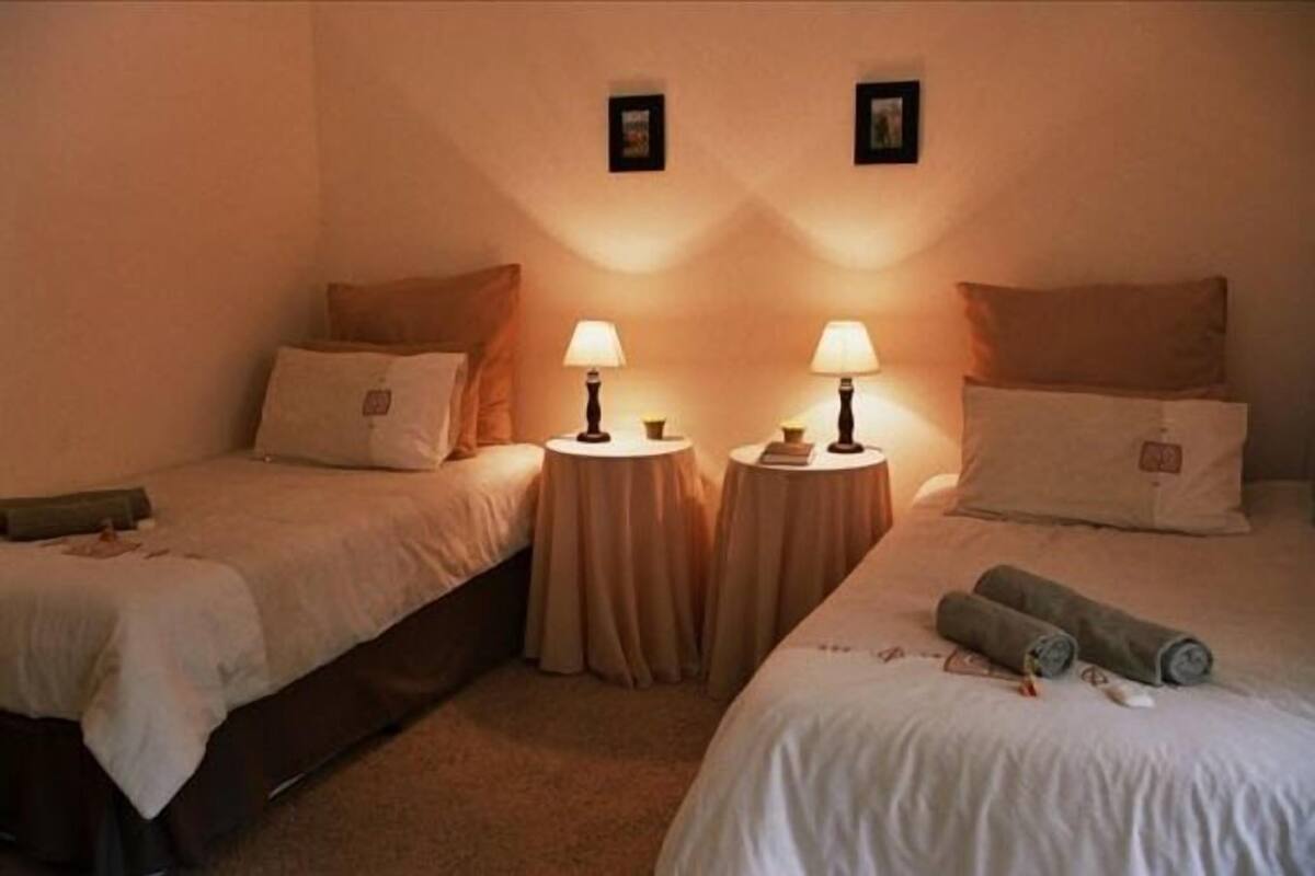 A hotel room with two single beds, each with a bedside table and lamp.
