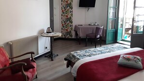 A hotel room with a bed, a desk, a chair, a radiator, a TV, and a window with a view of the outside. - Le Madelon (Pays-de-Belves)
