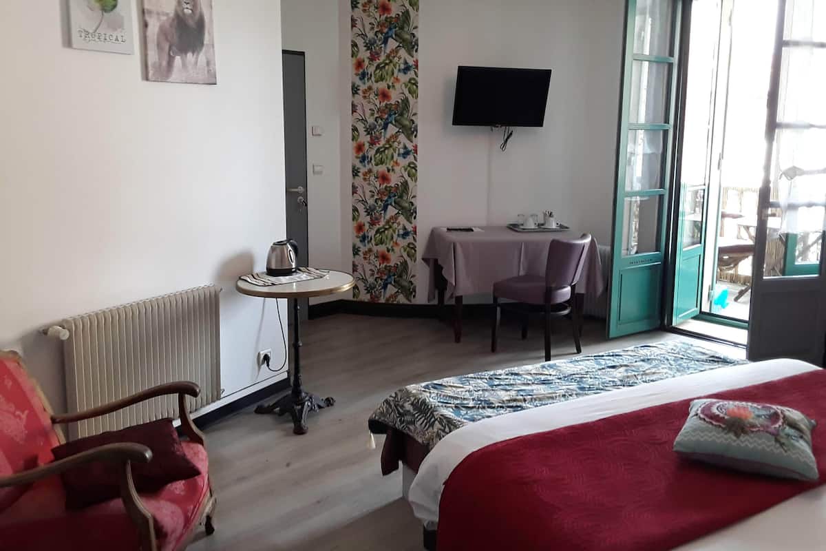 A hotel room with a bed, a desk, a chair, a radiator, a TV, and a window with a view of the outside.