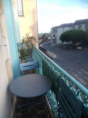 Ein Balkon mit Tisch und Stühlen, der auf eine Straße mit Gebäuden und einem Baum blickt.