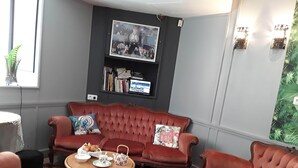A cozy room with a red sofa, a small table with tea set, and a bookshelf. - Le Madelon (Pays-de-Belves)