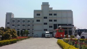 Un edificio de varios pisos con un letrero que dice "The Vaishali Residency". Varias unidades de transporte, incluyendo un autobús rojo y una camioneta blanca, están estacionadas adelante.