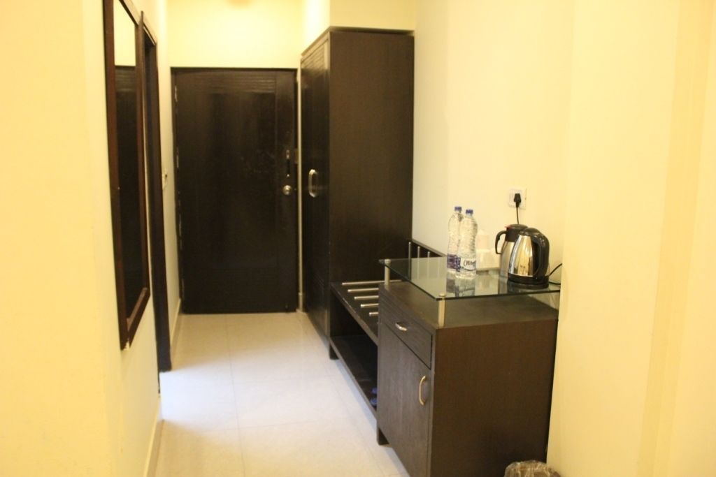 A narrow hallway with a dark wooden door at the end, a small kitchenette with a coffee maker, and a water dispenser on the counter.