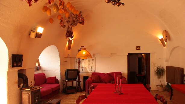 Un comedor acogedor con una mesa larga, mantel rojo y velas. Hay un sofá y una televisión en la esquina.