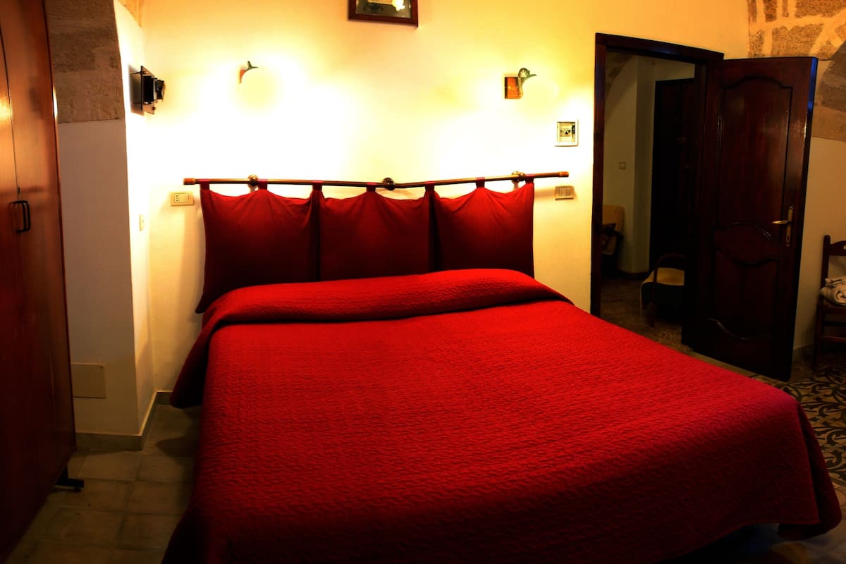 A hotel room with a large bed, a wooden headboard, and a door leading to another room.