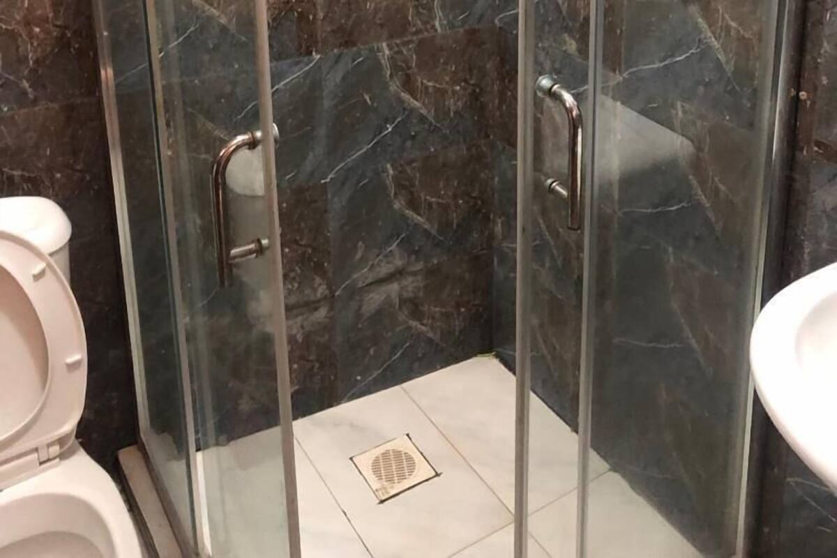 A glass-enclosed shower stall with a marble wall, a toilet, and a sink.