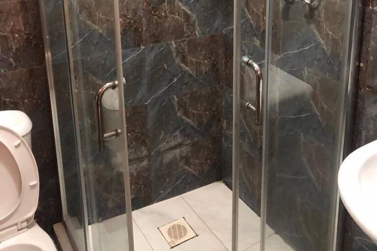 A glass-enclosed shower stall with a marble wall, a toilet, and a sink.