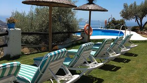 A poolside area with lounge chairs and umbrellas, a clear view of the ocean, and a lifebuoy by the pool. - Hotel Rural Los Caracoles (Torrox)