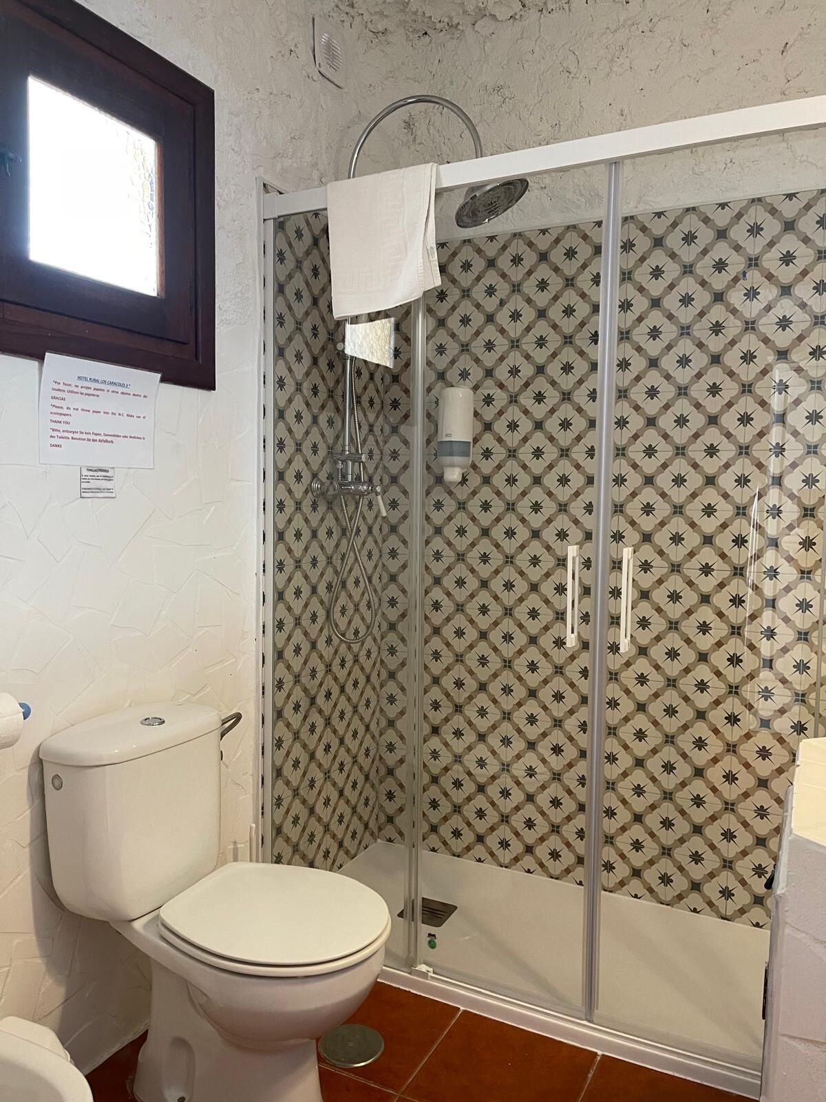 Un bany amb vàter, dutxa amb porta de vidre i rajoles amb dibuixos.