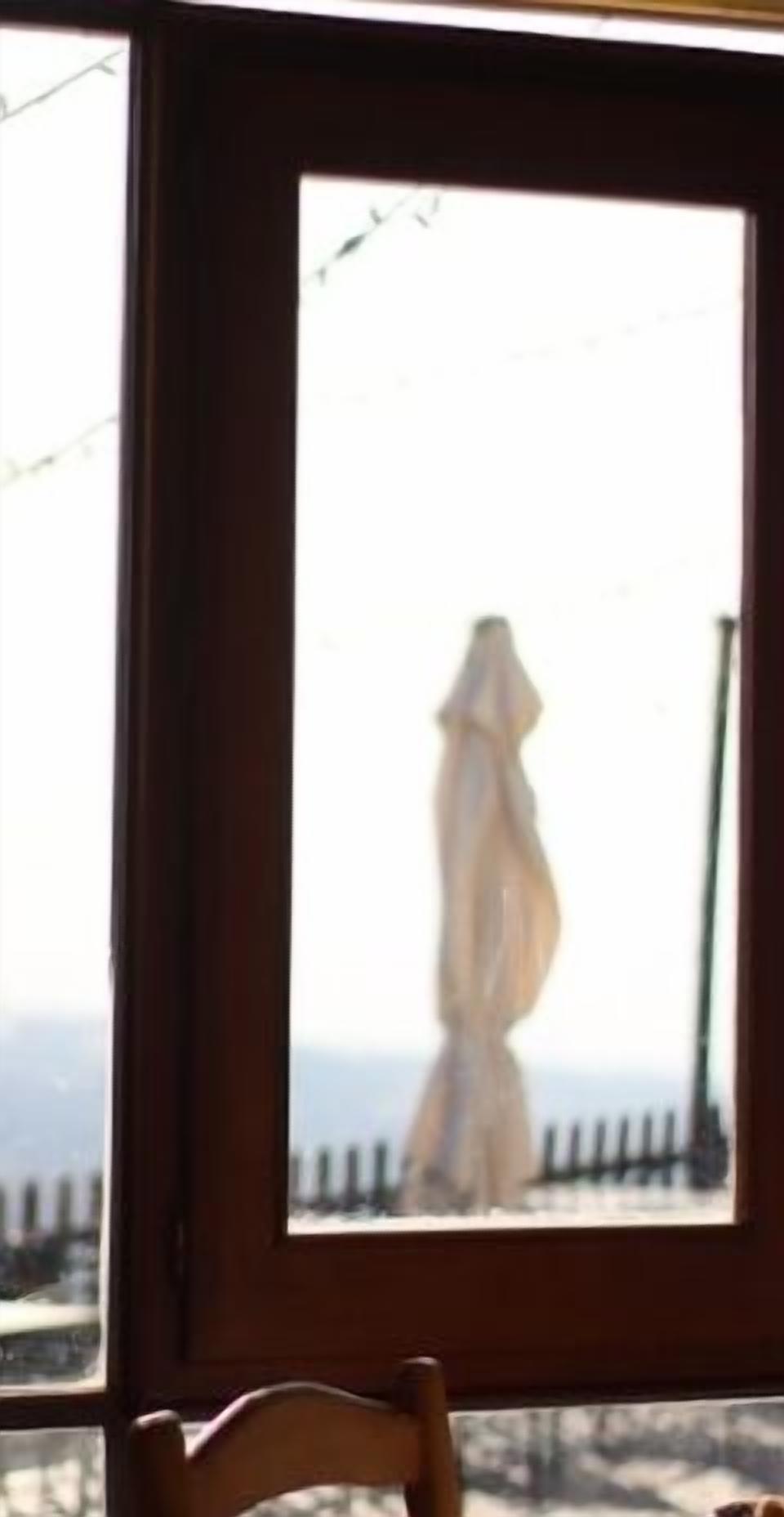 A window with a view of a fence and a blurred figure in the distance.
