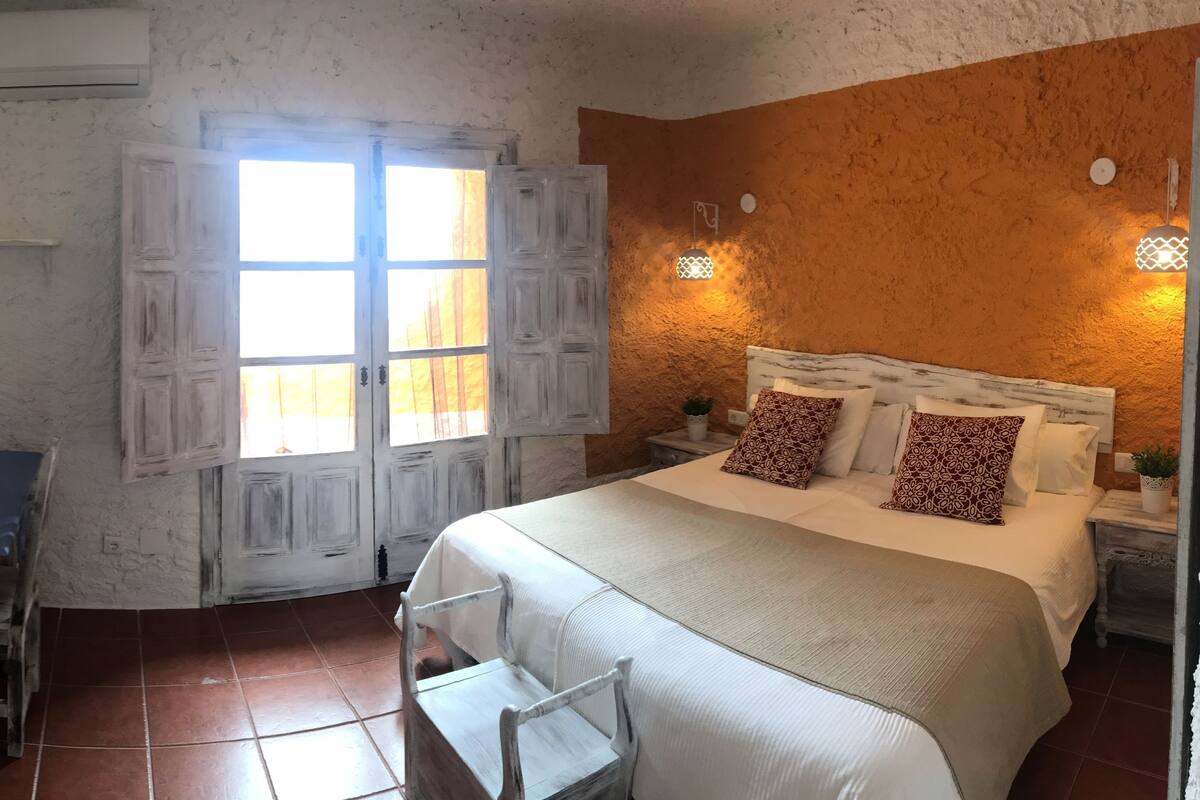 Een slaapkamer met een bed, een bureau, een stoel en een raam met gordijnen.