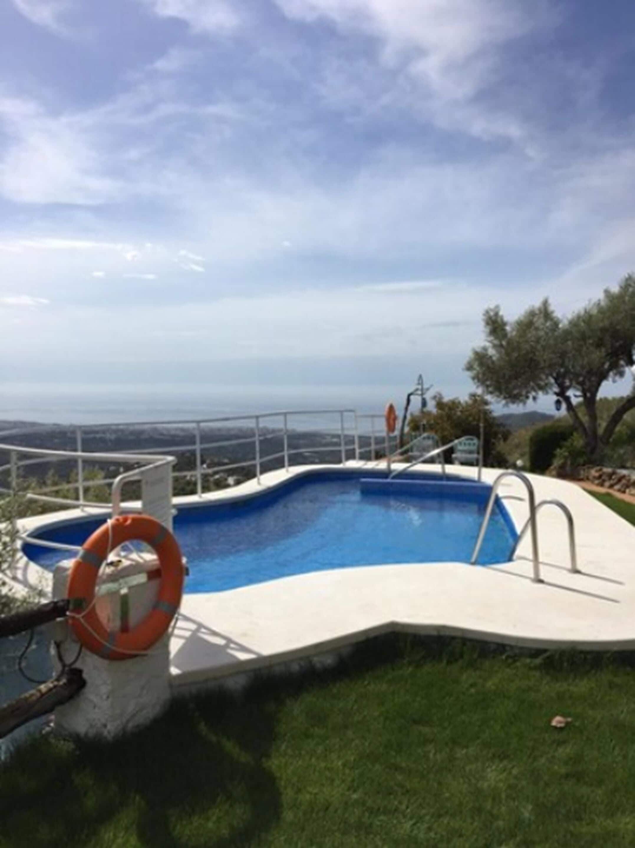 A swimming pool with a lifebuoy, surrounded by a white deck and a metal railing.