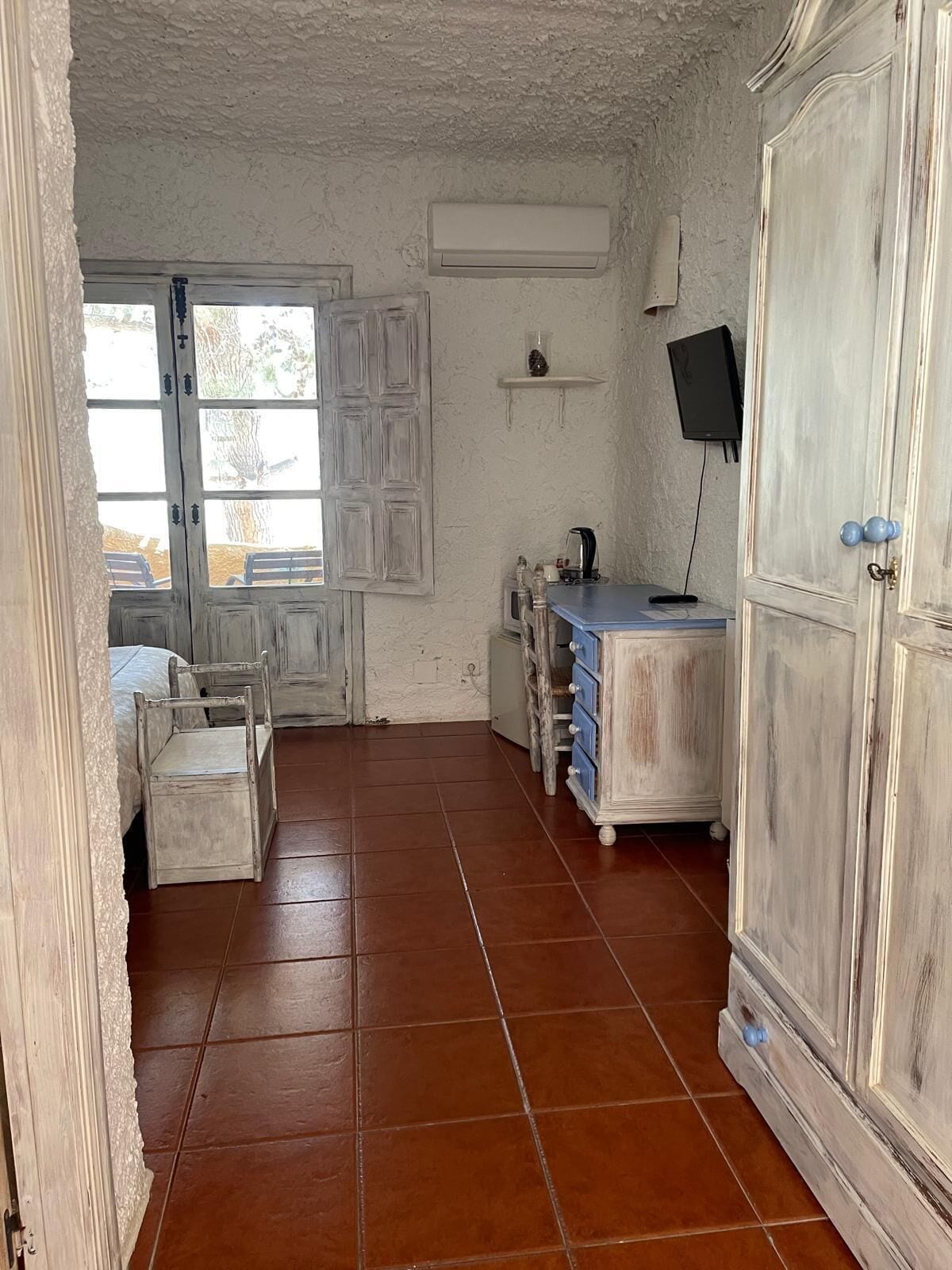 Une pièce rustique avec un meuble en bois, une petite table avec des tiroirs, une chaise et un téléviseur fixé au mur.