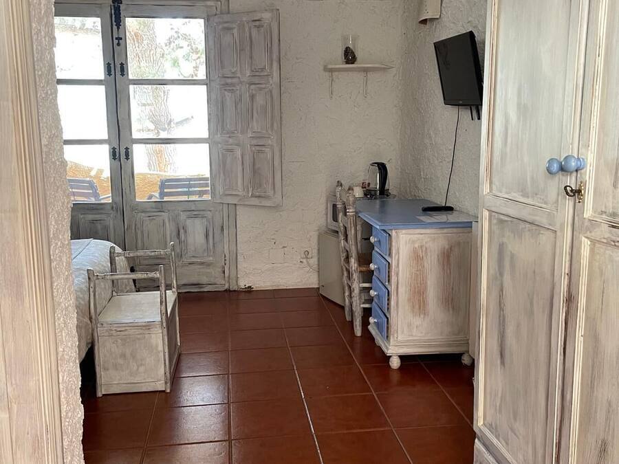 Une pièce rustique avec un meuble en bois, une petite table avec des tiroirs, une chaise et un téléviseur fixé au mur.