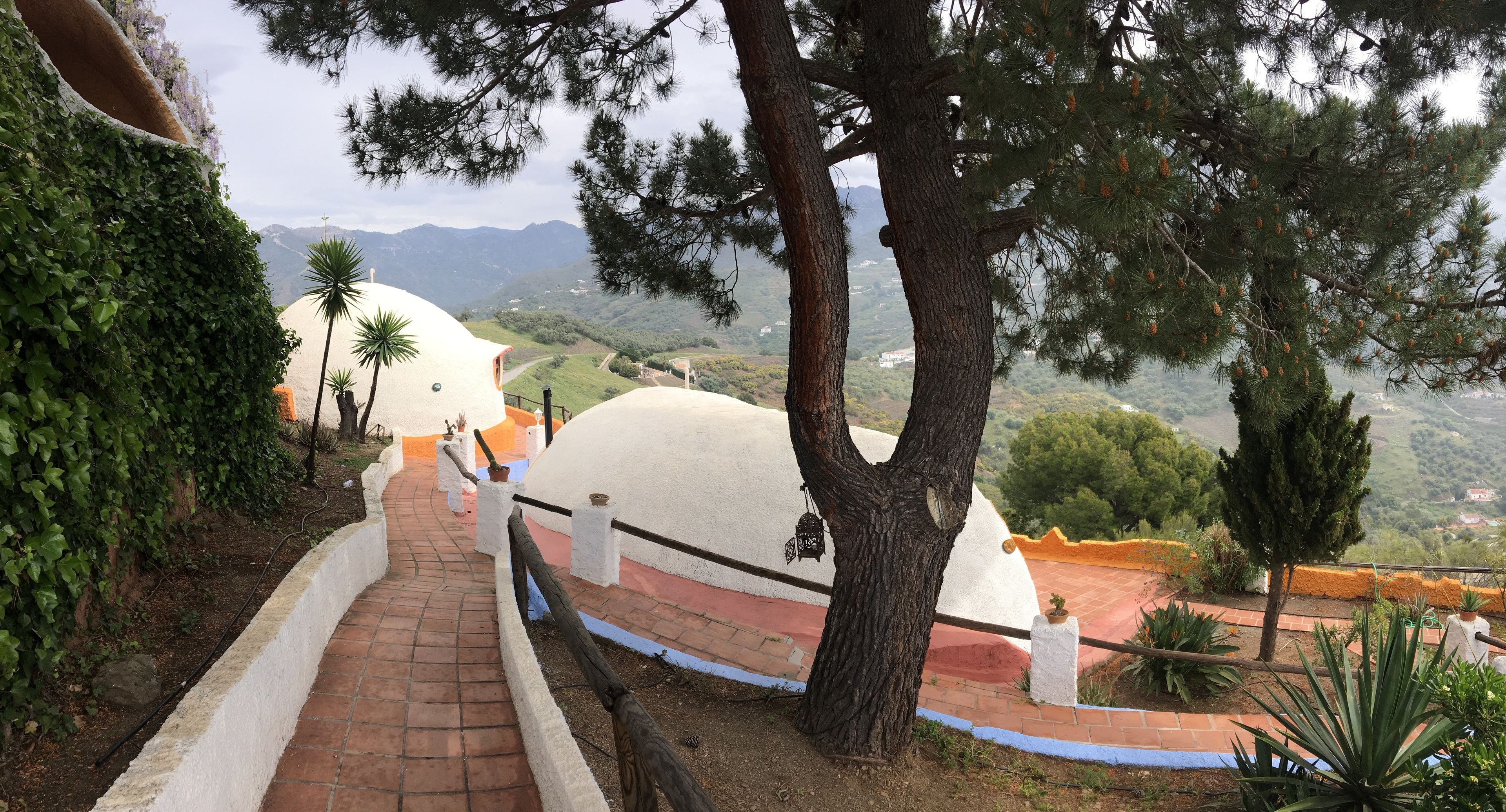 A pathway leading to a white dome-shaped building with a red roof, surrounded by trees and a mountainous landscape.