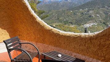 A terrace with two black metal chairs and a table, overlooking a mountainous landscape with buildings.