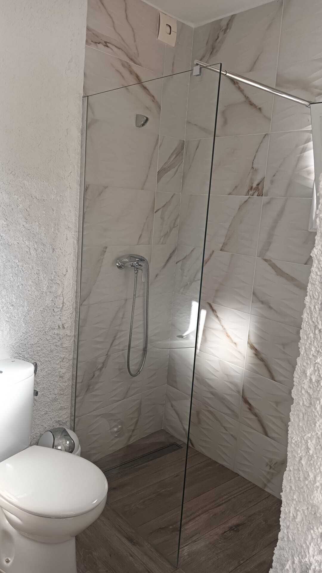 Un baño con ducha vidriada, inodoro y paredes con diseño de mármol.