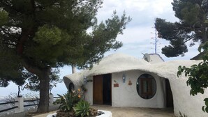 A rustic building with a thatched roof, a stone pathway, and a small garden with plants and a tree. - Hotel Rural Los Caracoles (Torrox)