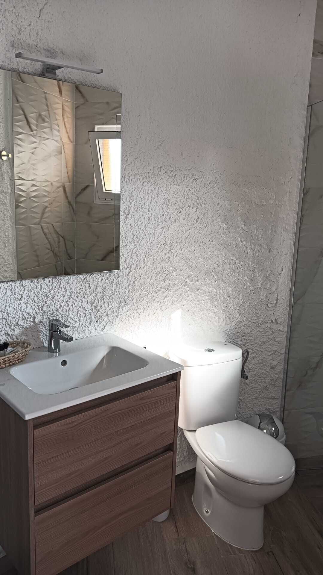 A bathroom with a white sink, wooden cabinet, and a toilet.