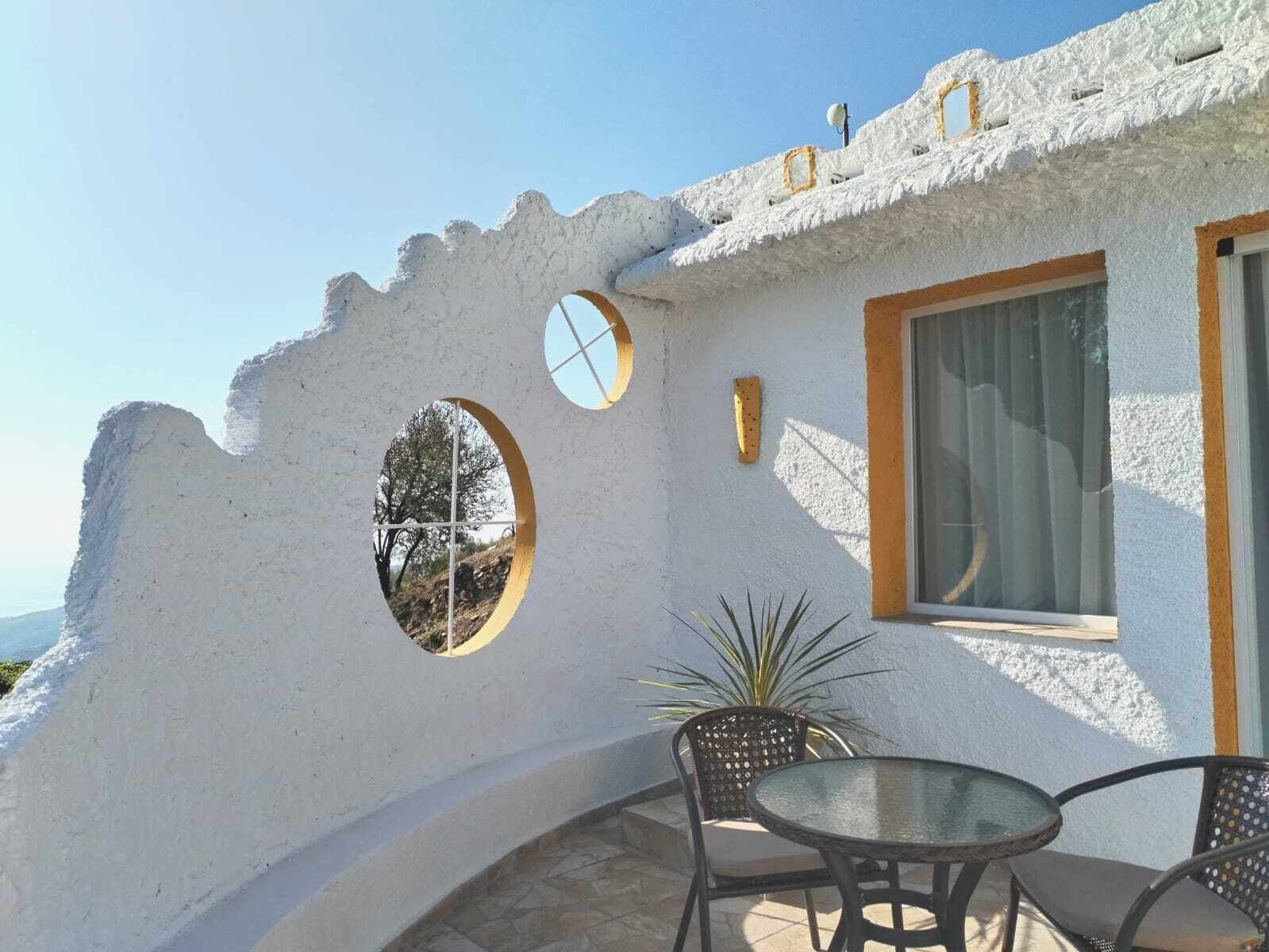A white building with a unique architectural design, featuring circular windows and a small patio area with a table and chairs.