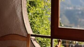 Un coin repas avec une table dressée pour deux personnes, et une vue sur la verdure et les montagnes par la fenêtre.