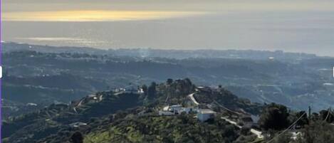 A mountainous landscape with a winding road, greenery, and distant buildings.