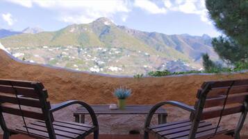 Dos sillas de madera mirando a una mesa con una planta en maceta, con vista a un paisaje montañoso.