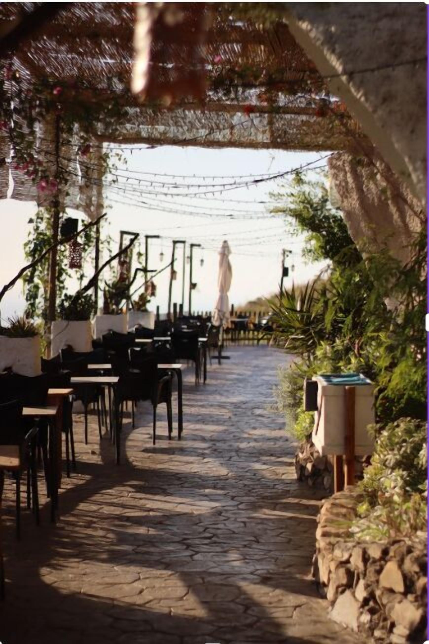An outdoor patio with stone flooring, tables, and chairs arranged for dining.