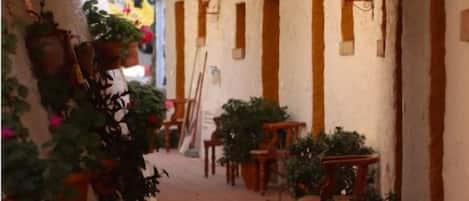 A narrow alleyway with terracotta tiles, wooden benches, and potted plants.