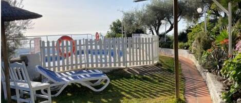 Un patio cubierto con valla blanca, un camino y sillones de descanso.