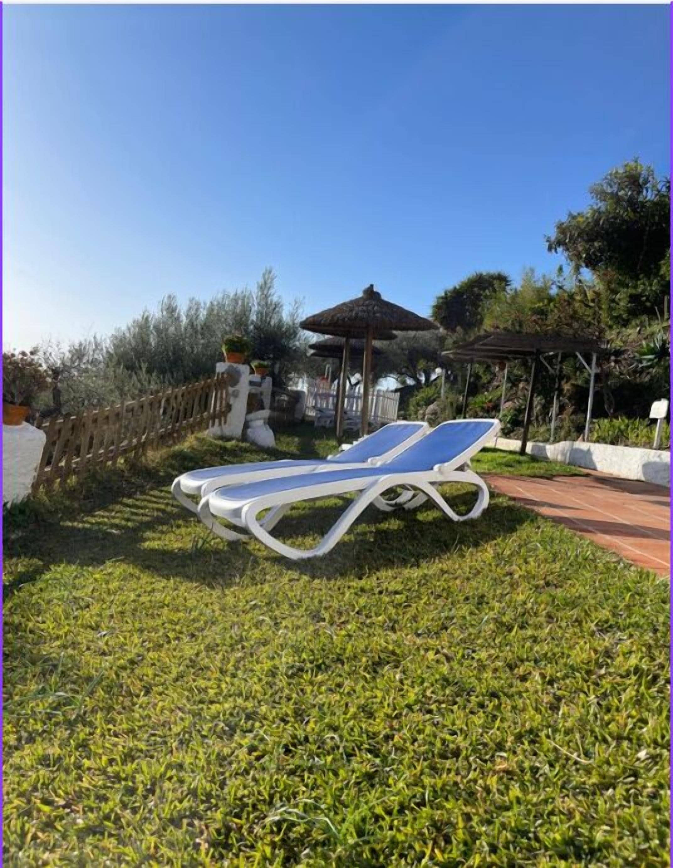 A sun lounger on a grassy lawn with a pergola and a gazebo in the background.