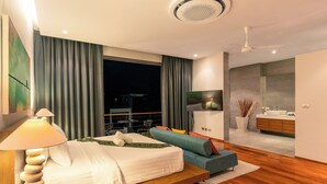 Ein modernes Hotelzimmer mit Bett, Sofa, Fernseher, Bad und Blick auf die nächtliche Stadt.