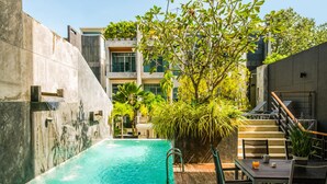 Ein Pool mit Holzterrasse, umgeben von üppiger Vegetation und einer Treppe, die zu einer höheren Ebene führt.