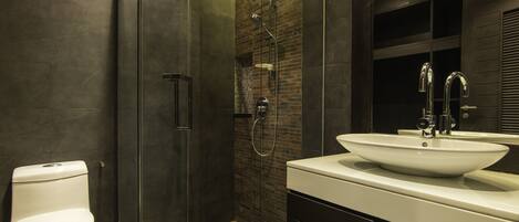 Un baño moderno con ducha de vidrio, lavamanos blanco y azulejos en tonos oscuros.