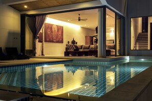 An indoor swimming pool with a glass enclosure, a ceiling fan, and a view into a living area with a sofa and a painting. - Amazing 5BR Seaview Private Pool Villa by Intira Villas (Rawai)