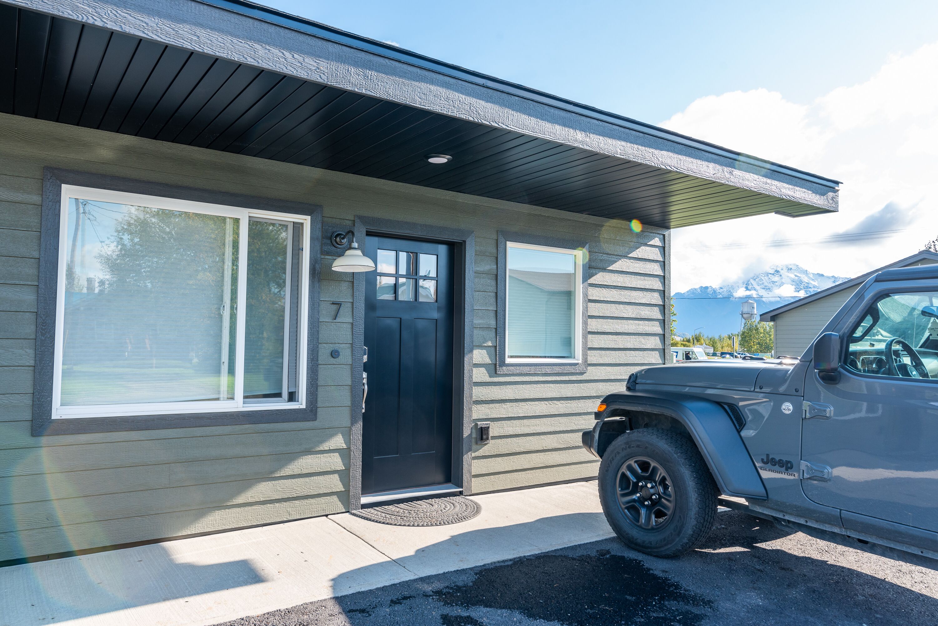 Een huis met een zwarte deur, twee ramen en een Jeep die ervoor geparkeerd staat.
