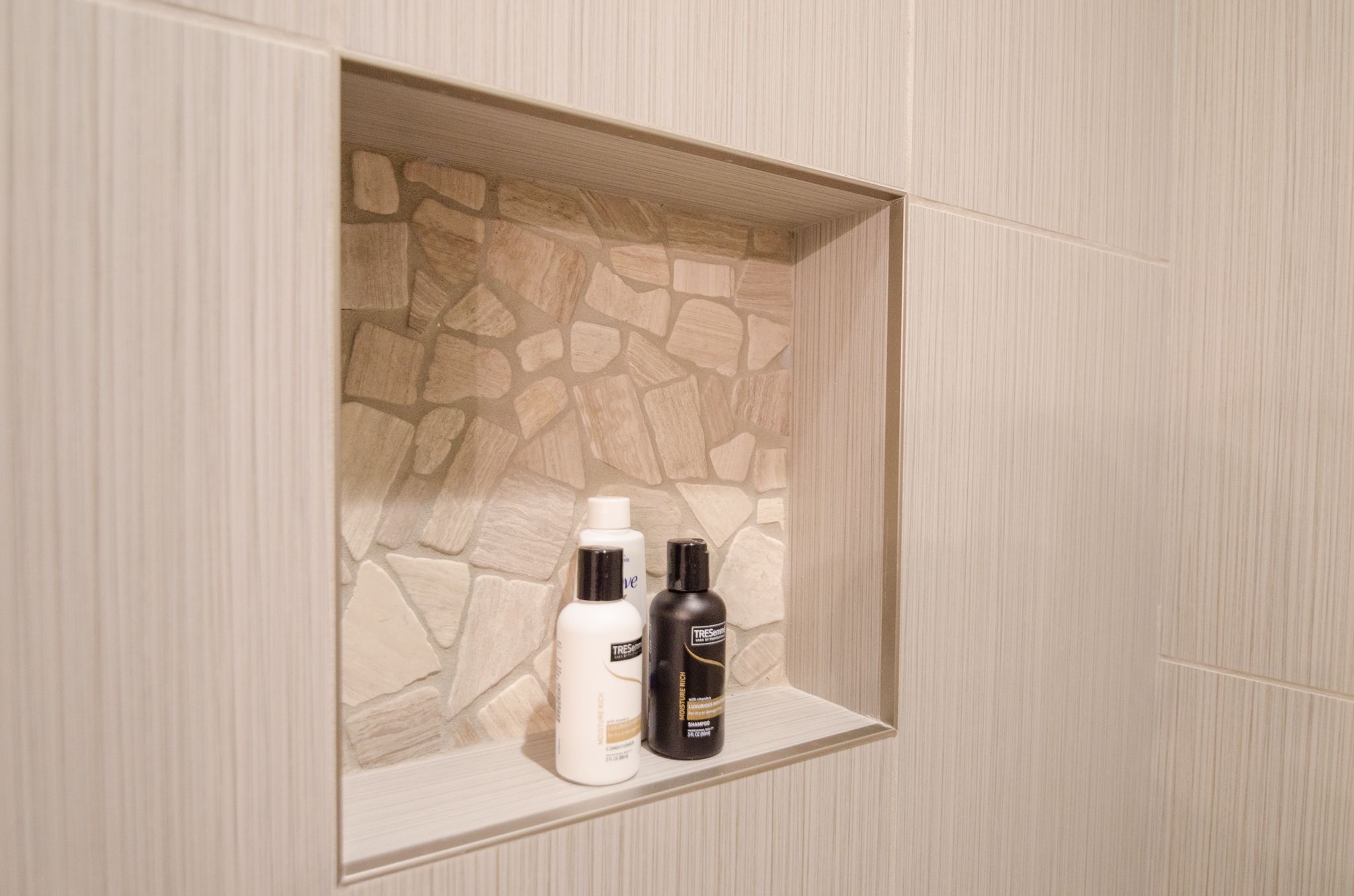 A bathroom with a stone wall and a shelf containing two toiletries.