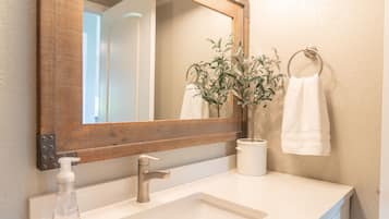 Un baño con espejo de marco de madera, lavabo blanco, dispensador de jabón y planta en maceta.
