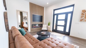 A modern living room with a large brown sectional sofa, a flat-screen TV mounted on a wooden panel, and a black coffee table.