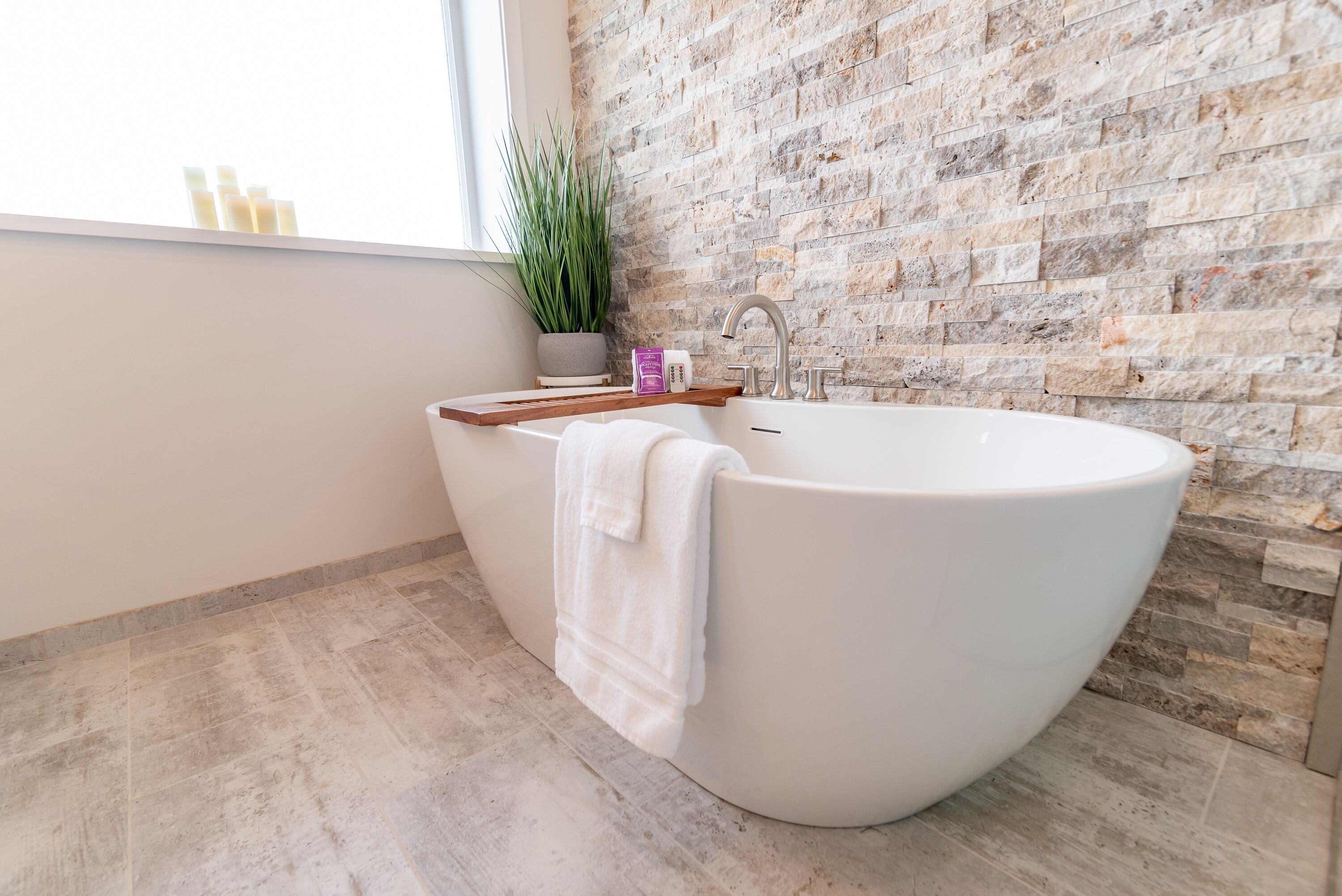 Un bagno moderno con una grande vasca freestanding, uno scaffale in legno, una pianta in vaso e una parete in mattoni.