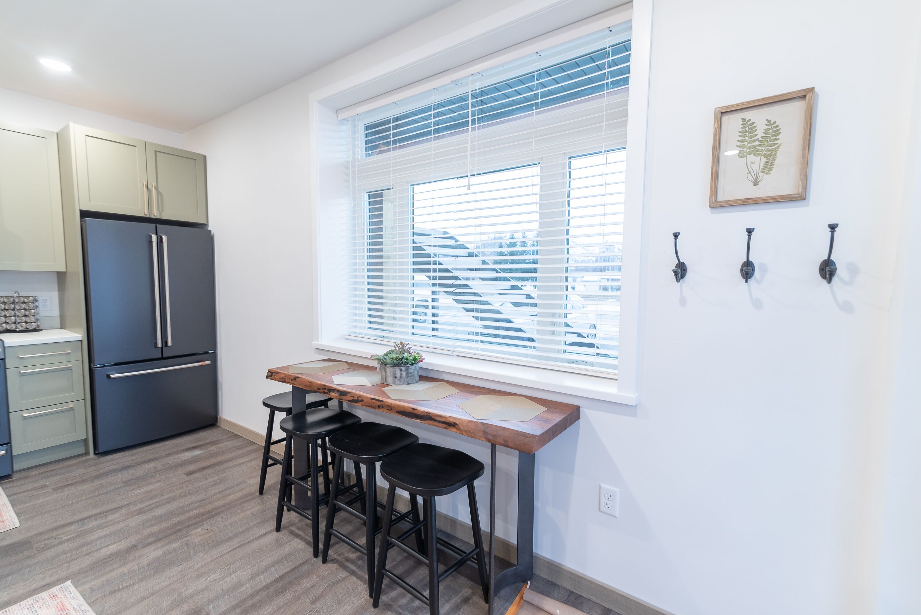 A modern kitchen with a built-in refrigerator, a wooden bar counter with stools, and a window with blinds.